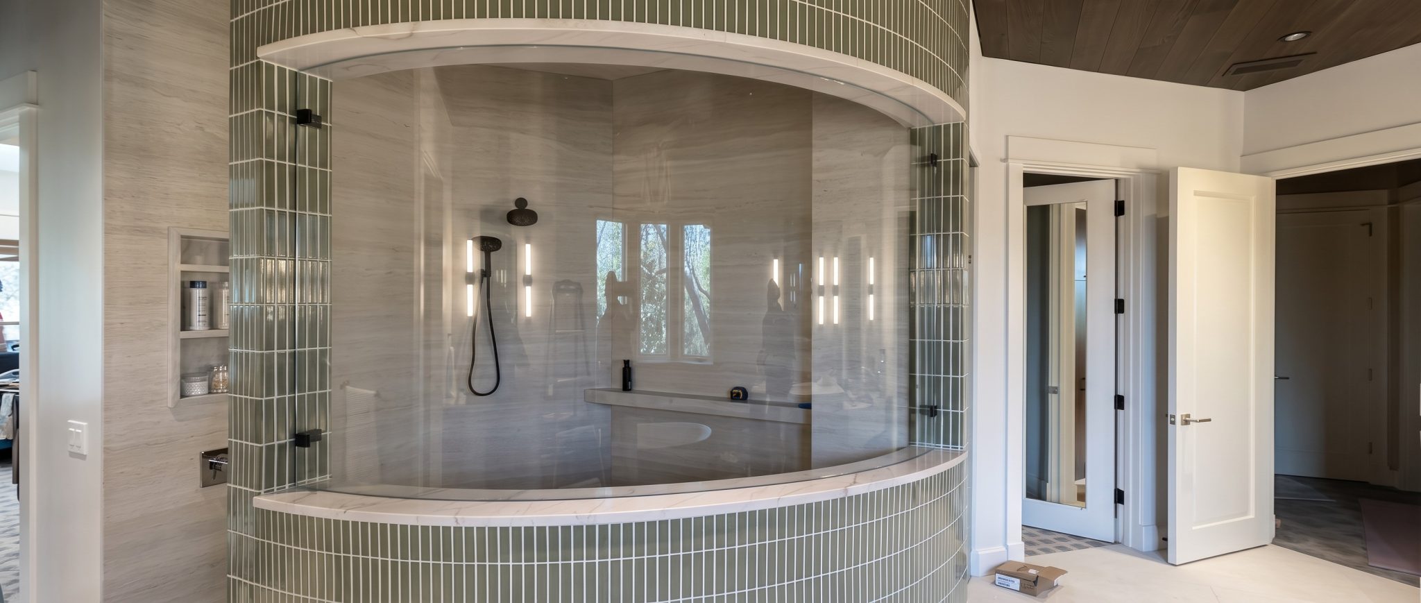 Curved frameless glass shower enclosure wrapped in stacked tile
