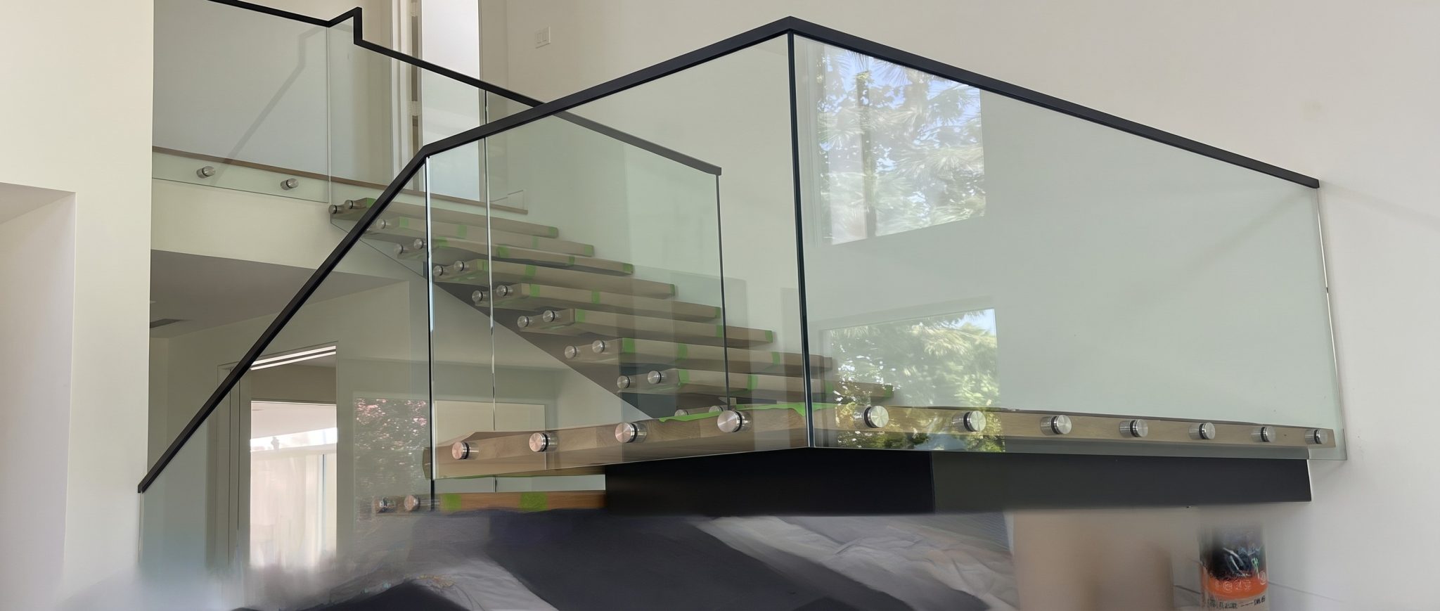 Frameless glass stair railing with a black metal cap and floating oak treads