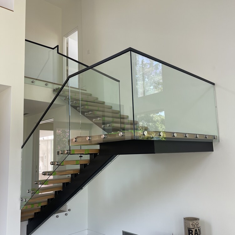 Frameless Glass Stair Railing Frameless glass stair railing with a black cap rail and floating oak treads