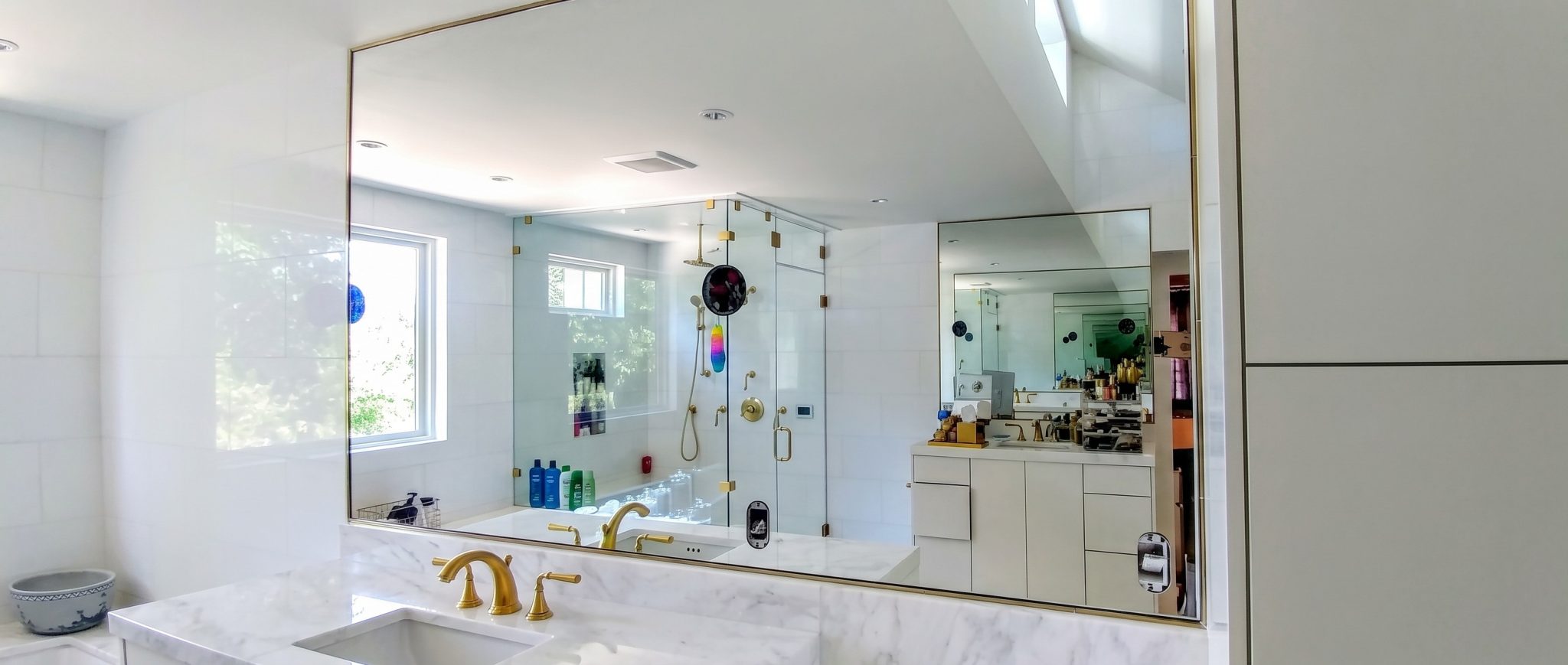 Large frameless wall mirror with polished edges above a marble vanity