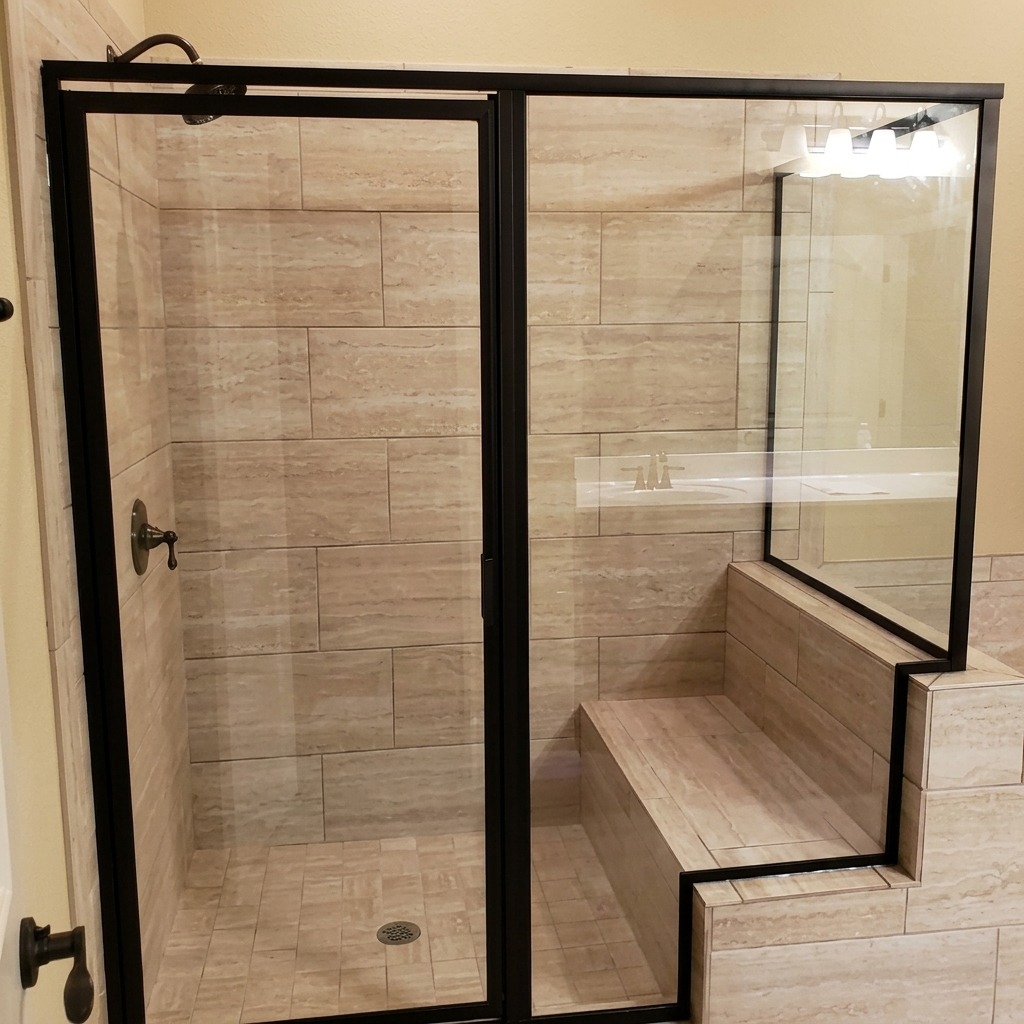 Framed glass shower enclosure with black hardware and a tiled bench installed by Shower Doors of Austin