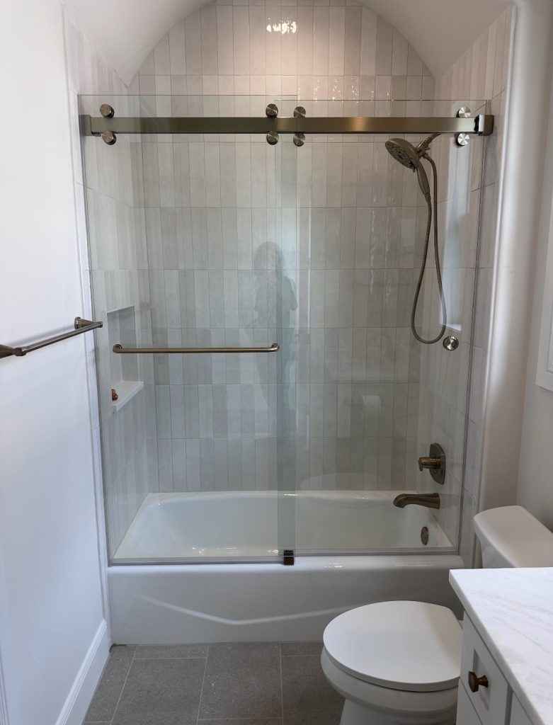 Frameless Cambridge sliding shower door with brushed bronze roller hardware over a tub in Austin, TX