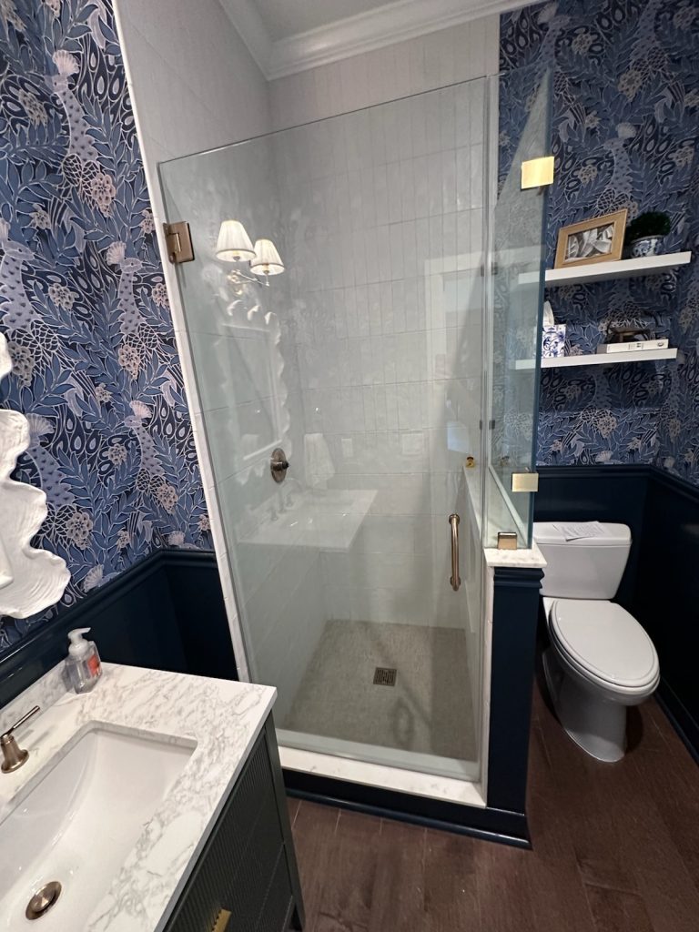 Custom frameless 90-degree shower enclosure with a partial pony wall and brushed bronze hardware in Austin, TX