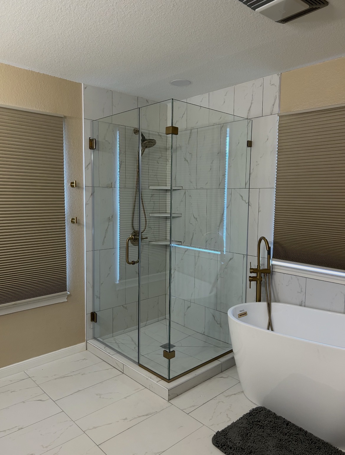 Custom 90-degree frameless shower enclosure with brushed gold hardware beside a freestanding tub in Kyle, TX