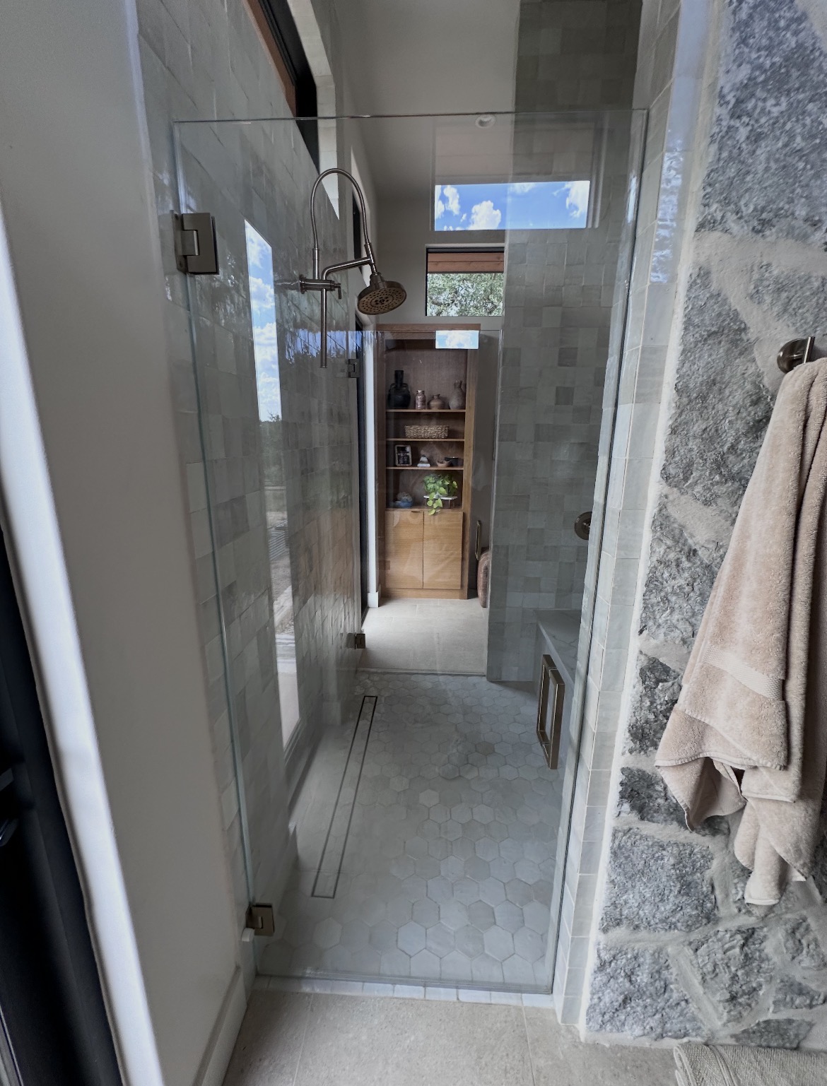 Walk-in shower with two frameless low-iron glass doors on either side of a natural stone wall in Wimberley, TX