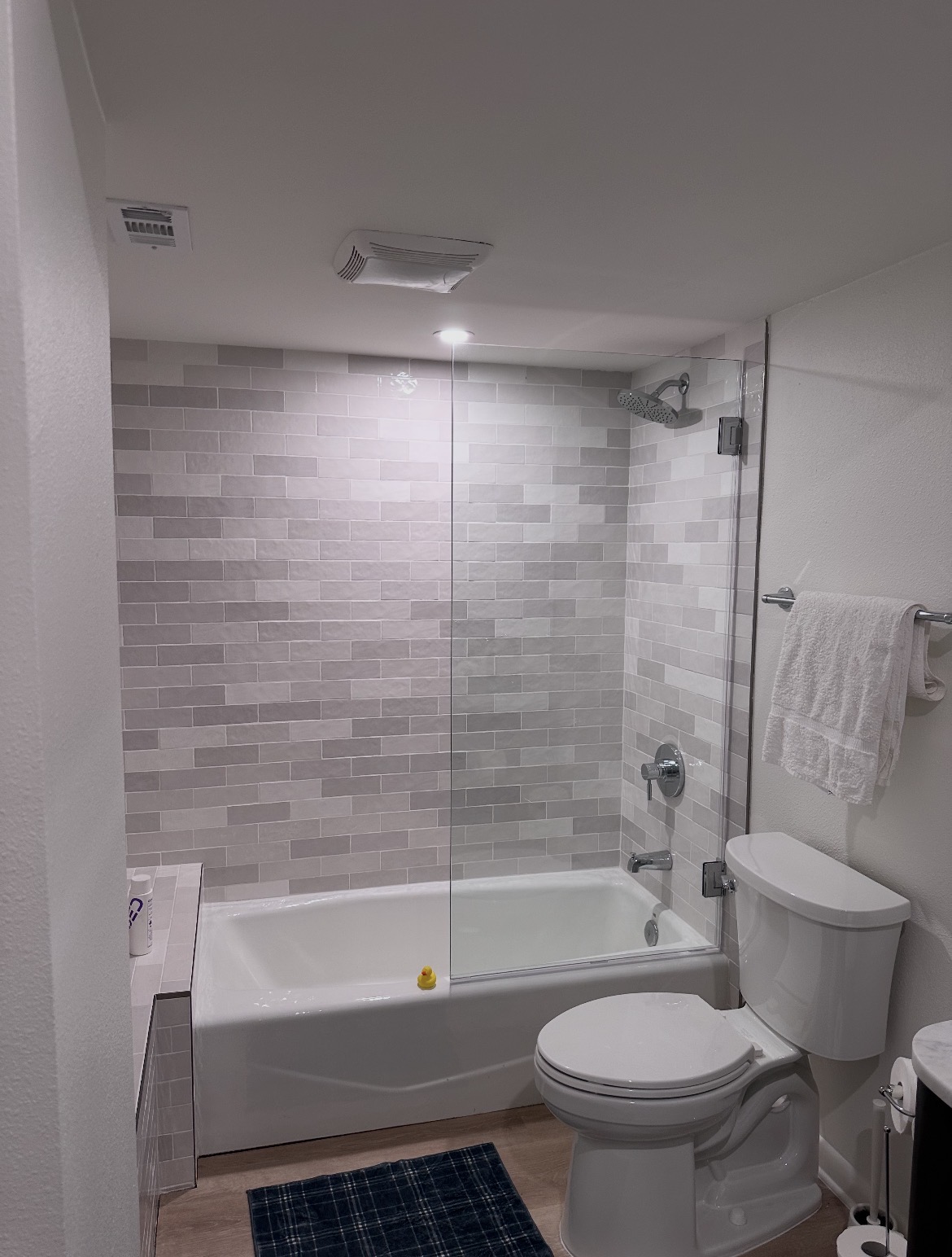Frameless glass splash panel with polished chrome hardware over a tub with gray subway tile in Austin, TX
