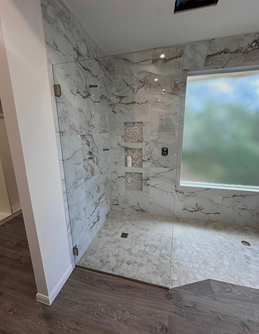 Low-iron glass splash panel with brushed bronze hardware in a marble walk-in shower in Austin, TX