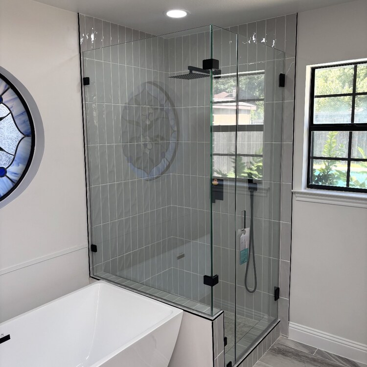 Frameless 90-degree glass shower with black hardware beside a freestanding tub