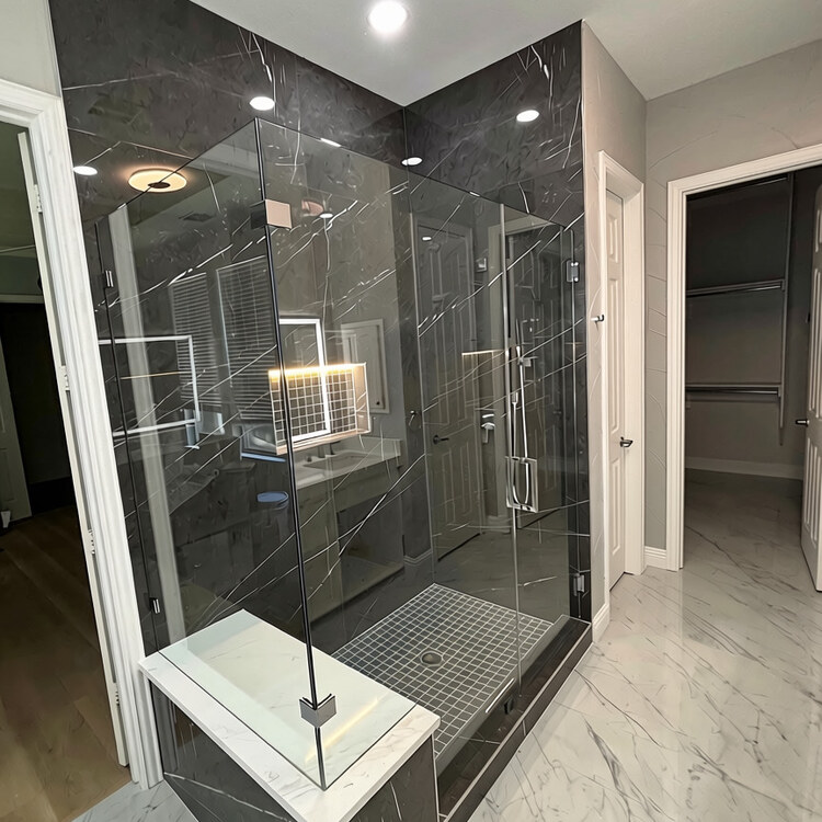 Corner view of a frameless glass enclosure with black marble walls and a white bench top