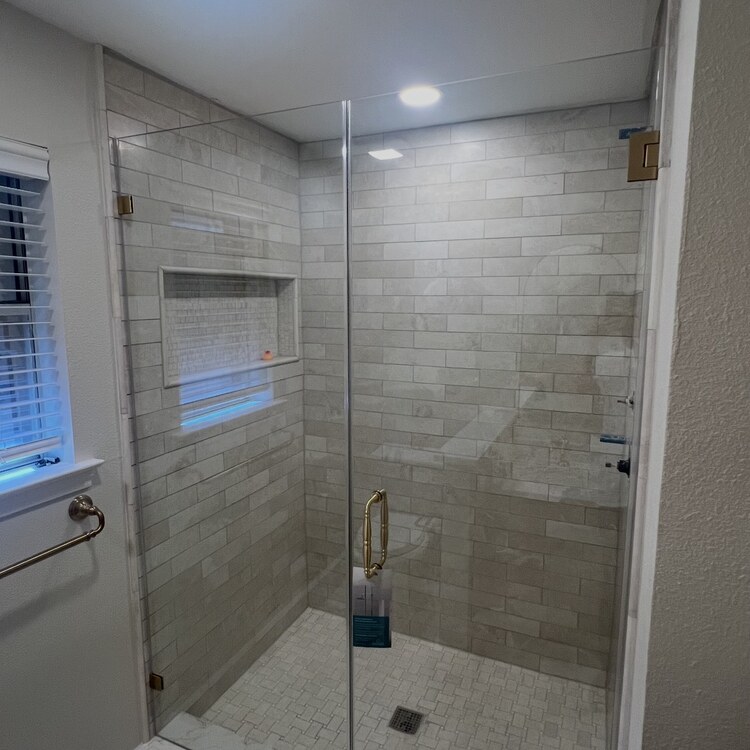 Frameless inline glass shower door with gold hinges and a tiled niche