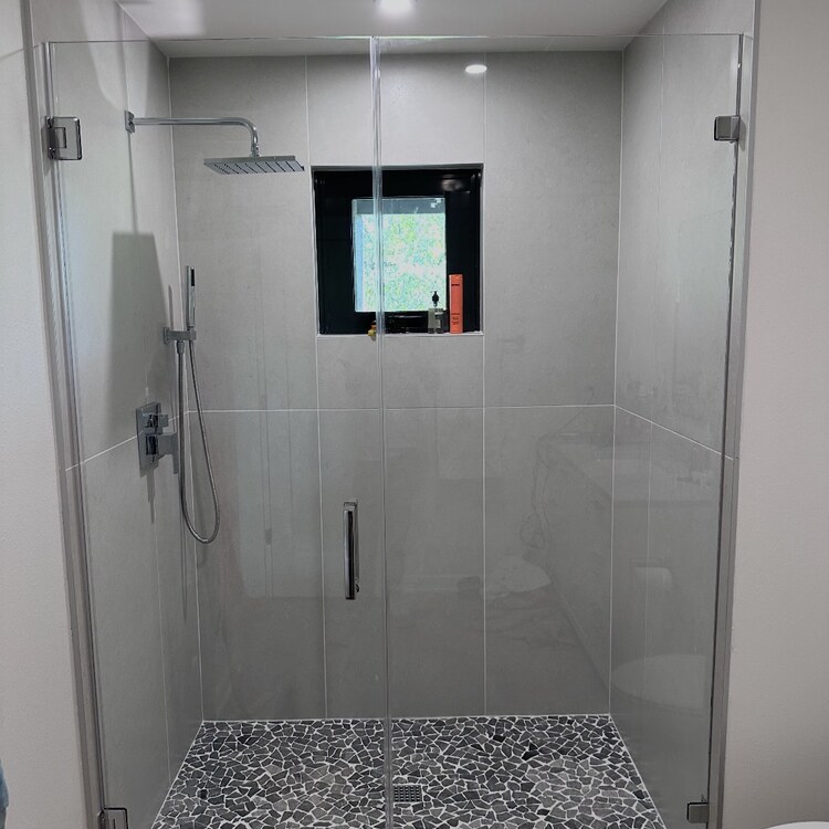 Frameless glass shower door and panels around a pebble tile shower floor