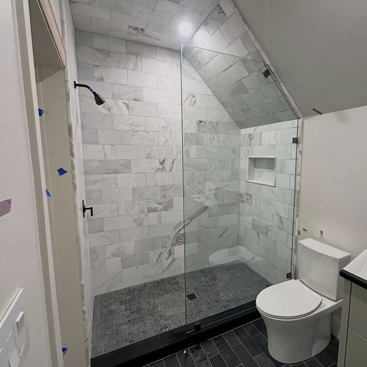 Frameless glass shower panel and door under a sloped bathroom ceiling